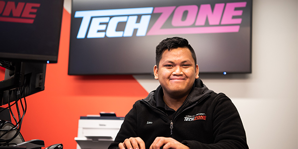 TechZone student sales associate standing behind the counter smiling